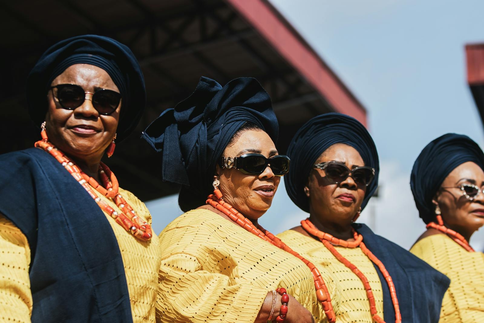 Women in traditional Yoruba attire, wearing vibrant gele and beads at a Nigerian cultural event.