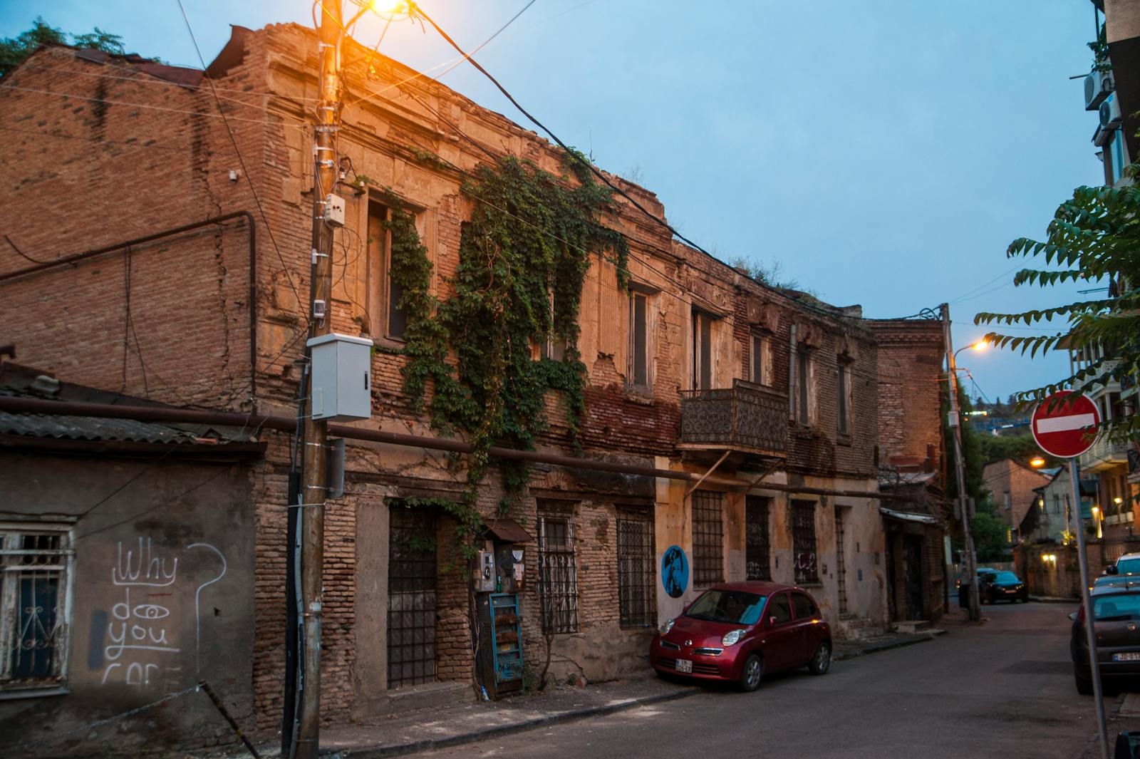 A rustic street in Tbilisi with old brick buildings and a vintage car at twilight.