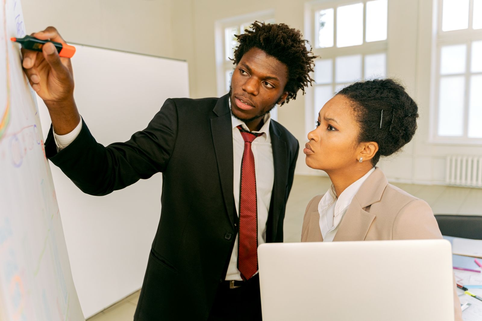 Two professionals brainstorm at a whiteboard in an office setting, fostering teamwork.
