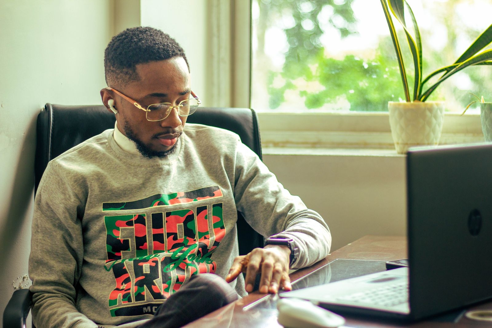 A young man in a home office, focused on his work using a laptop with natural light.