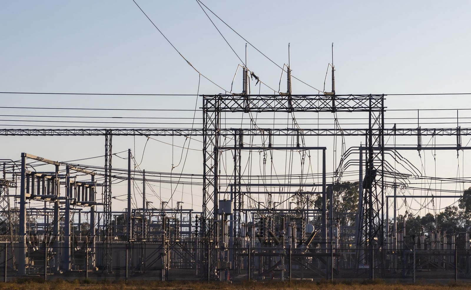 High-voltage electrical substation with steel structures and power lines at dawn.