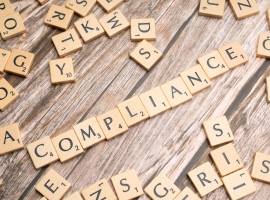Wooden letter tiles forming the word 'COMPLIANCE' on a rustic wooden background.