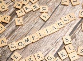 Wooden letter tiles forming the word 'COMPLIANCE' on a rustic wooden background.