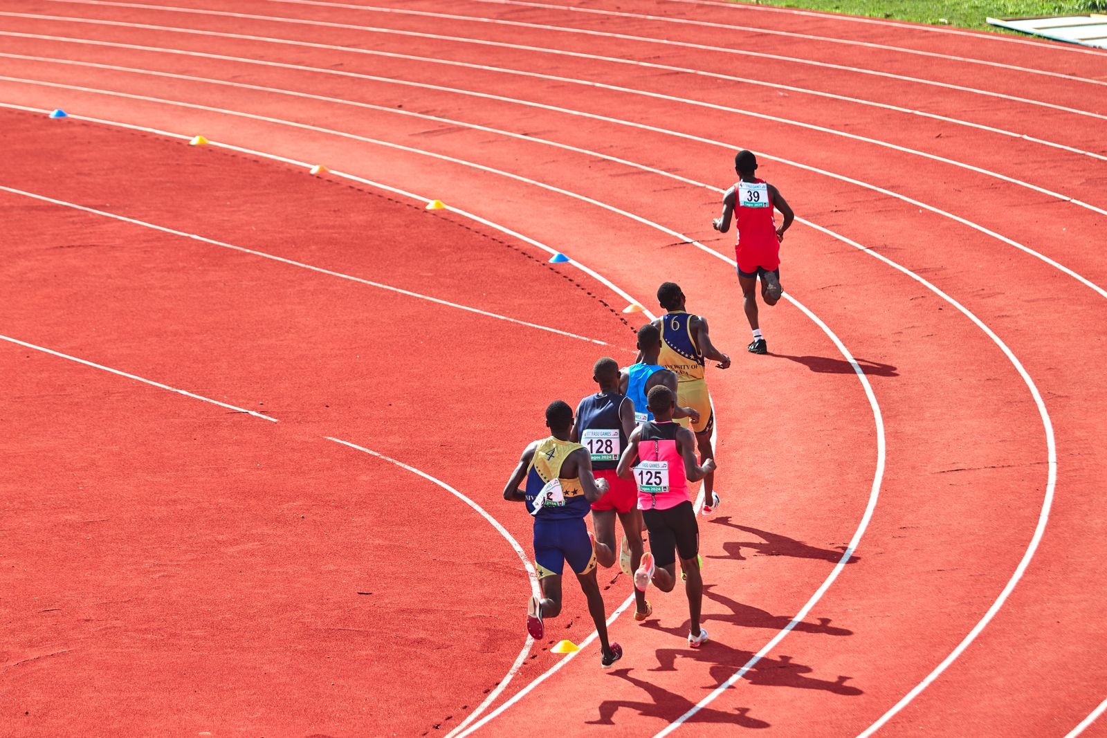 A group of athletes running on a curved outdoor track in a competitive race.