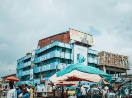 Lively street market scene in Kaduna, Nigeria, featuring vibrant Tecno Mobile advertising and local activity.