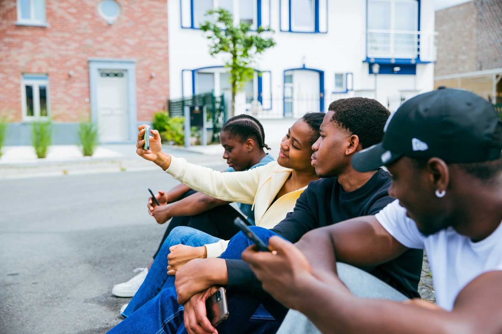 Four friends sitting outside in Brussels, capturing a selfie. Bright and lively scene.
