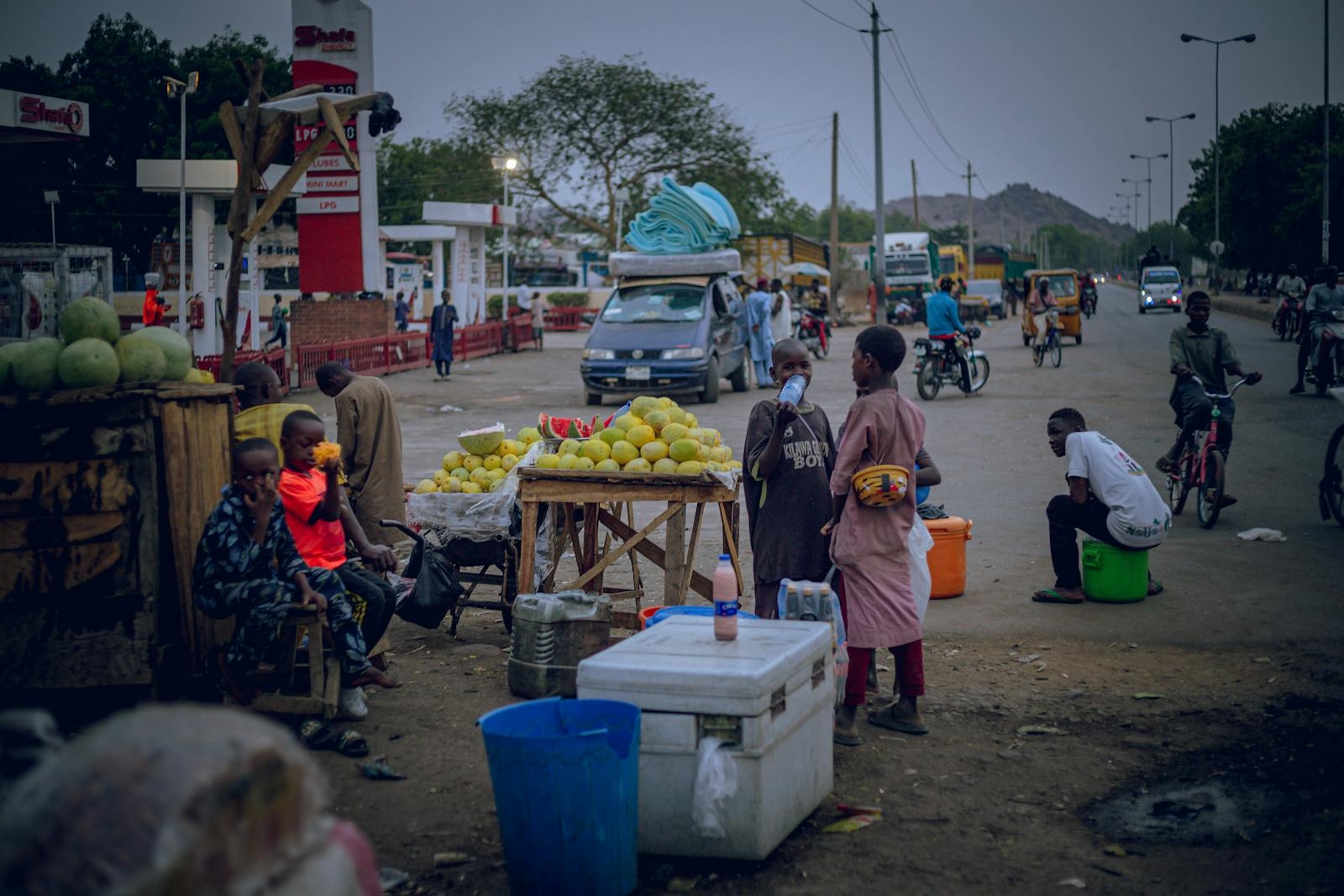 Vibrant street market in the evening with local vendors selling fruits and commuters passing by.