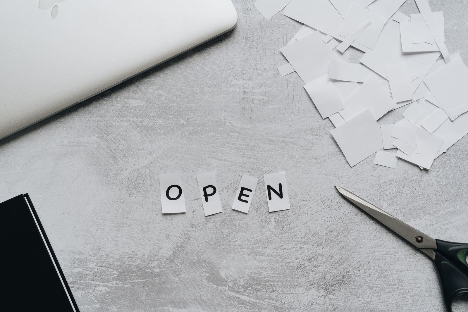 Flat lay of a creative workspace with paper letters spelling 'OPEN,' scissors, and a laptop.