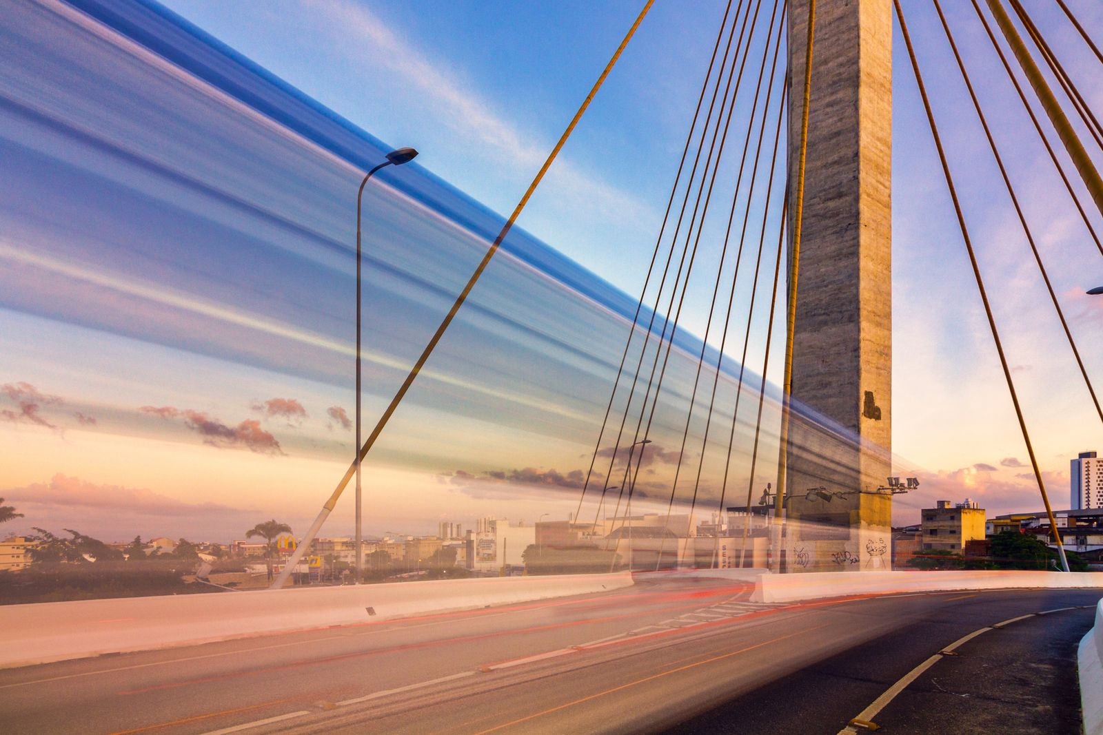 Long exposure photo capturing light trails on a modern urban bridge at twilight.