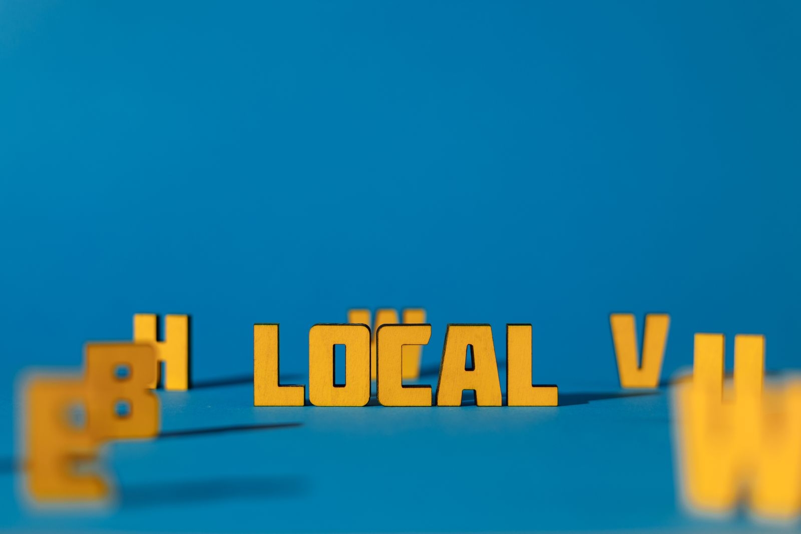 Abstract image featuring yellow wooden letters spelling 'LOCAL' on a blue background, offering ample copy space.