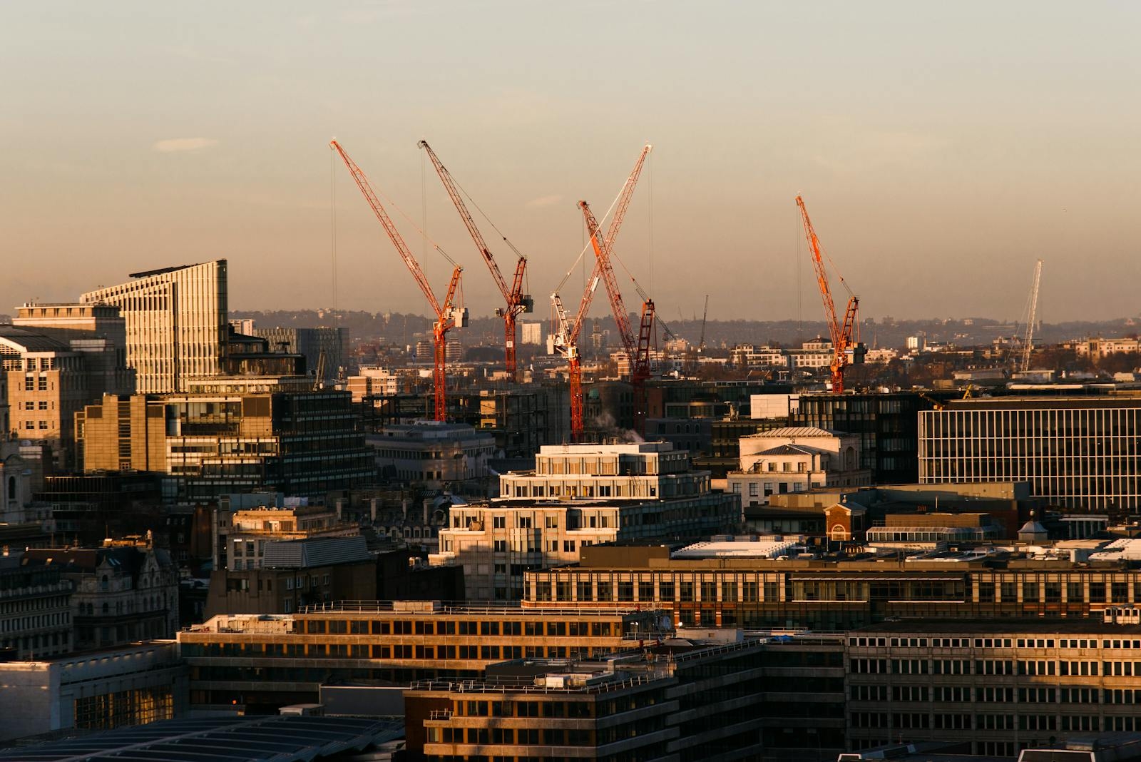 Cityscape of contemporary residential buildings with creative architecture near tall construction cranes located against cloudless sky on streets of modern city