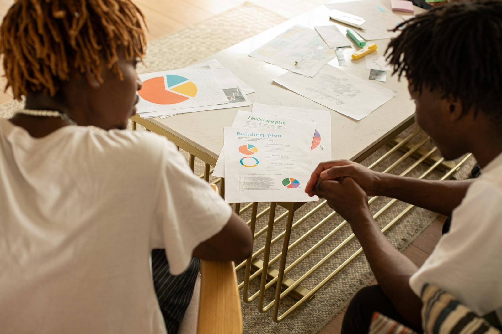 Two men collaborating over building plans at a desk, discussing data charts.