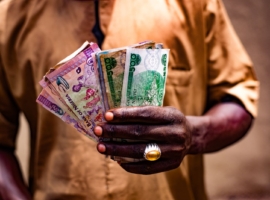 Close-up of a man holding Nigerian naira bills outdoors in Bida, Nigeria.