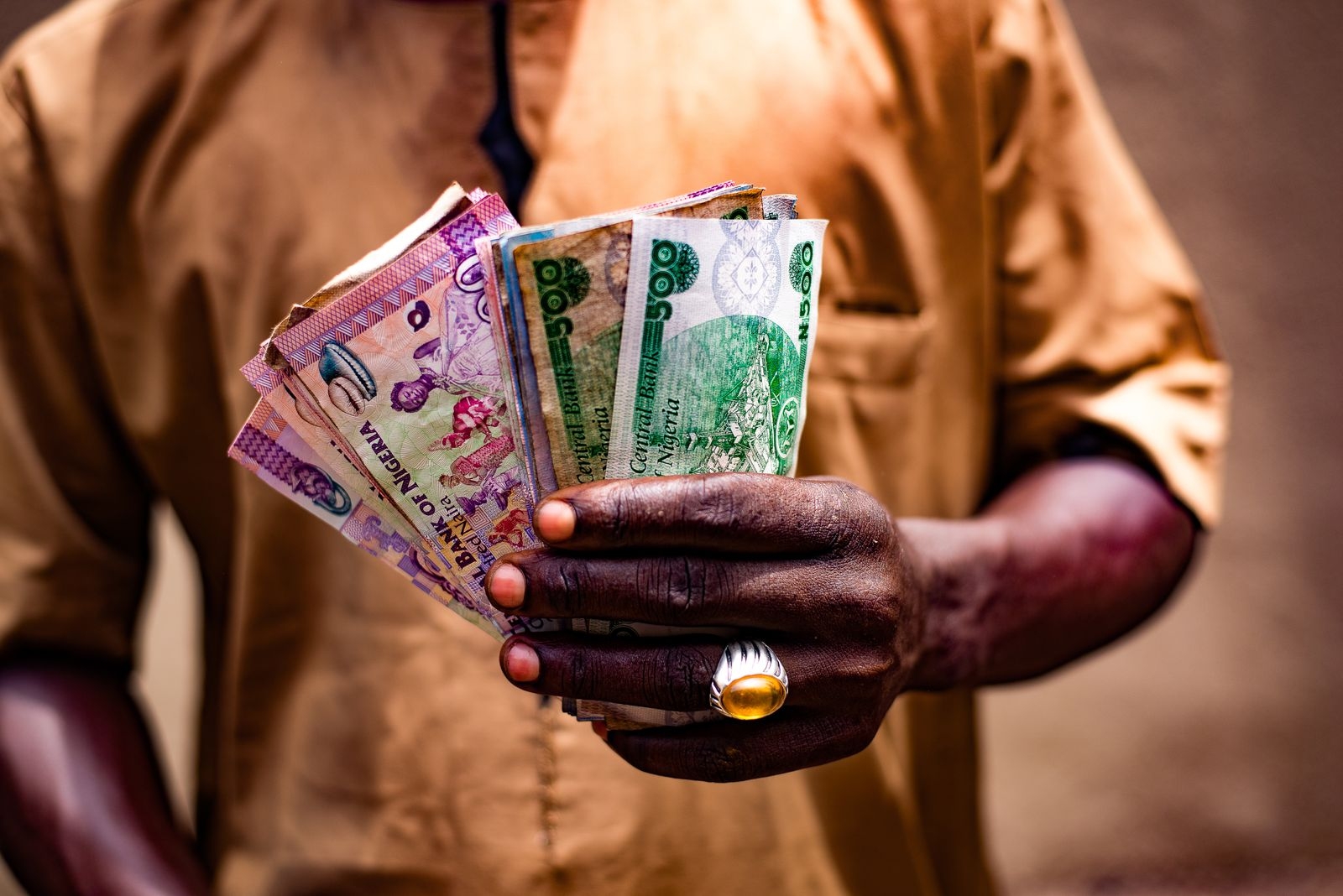 Close-up of a man holding Nigerian naira bills outdoors in Bida, Nigeria.